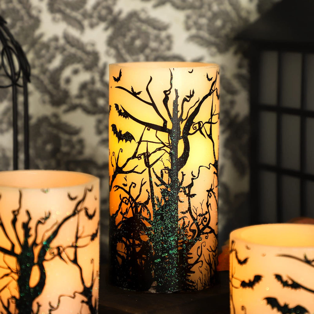 Three flameless LED pillar candles with black bat and tree decals, glowing from within, set on a shelf.