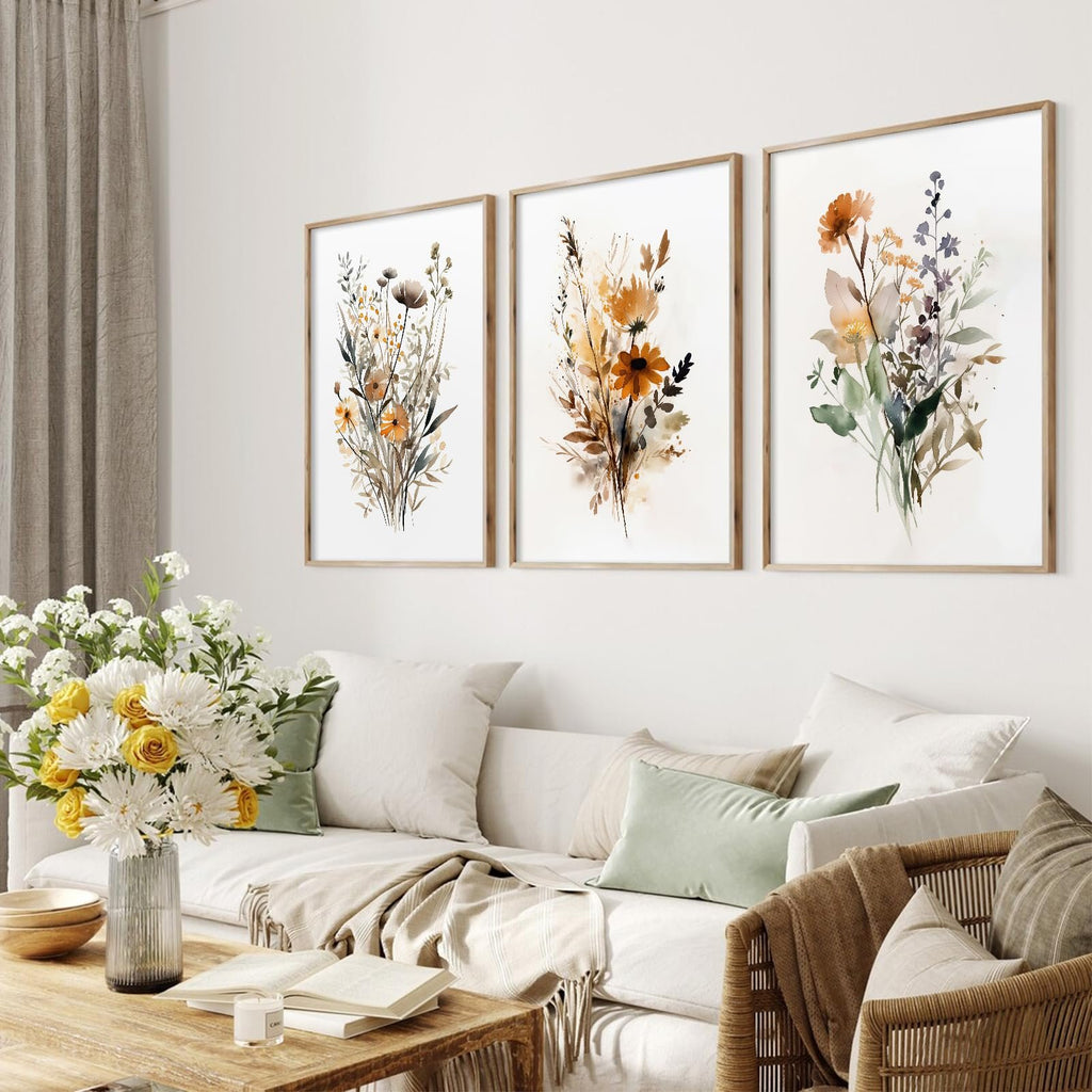 Three framed botanical wall art prints with watercolor wildflowers displayed above a sofa with decorative pillows and a coffee table.