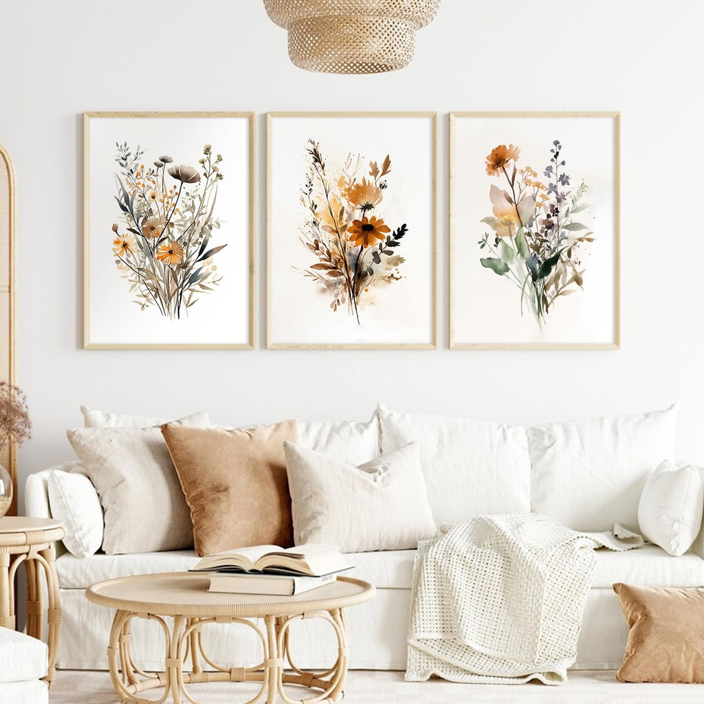 Three framed botanical watercolor prints of wildflowers displayed above a white sofa with decorative pillows and a woven coffee table.
