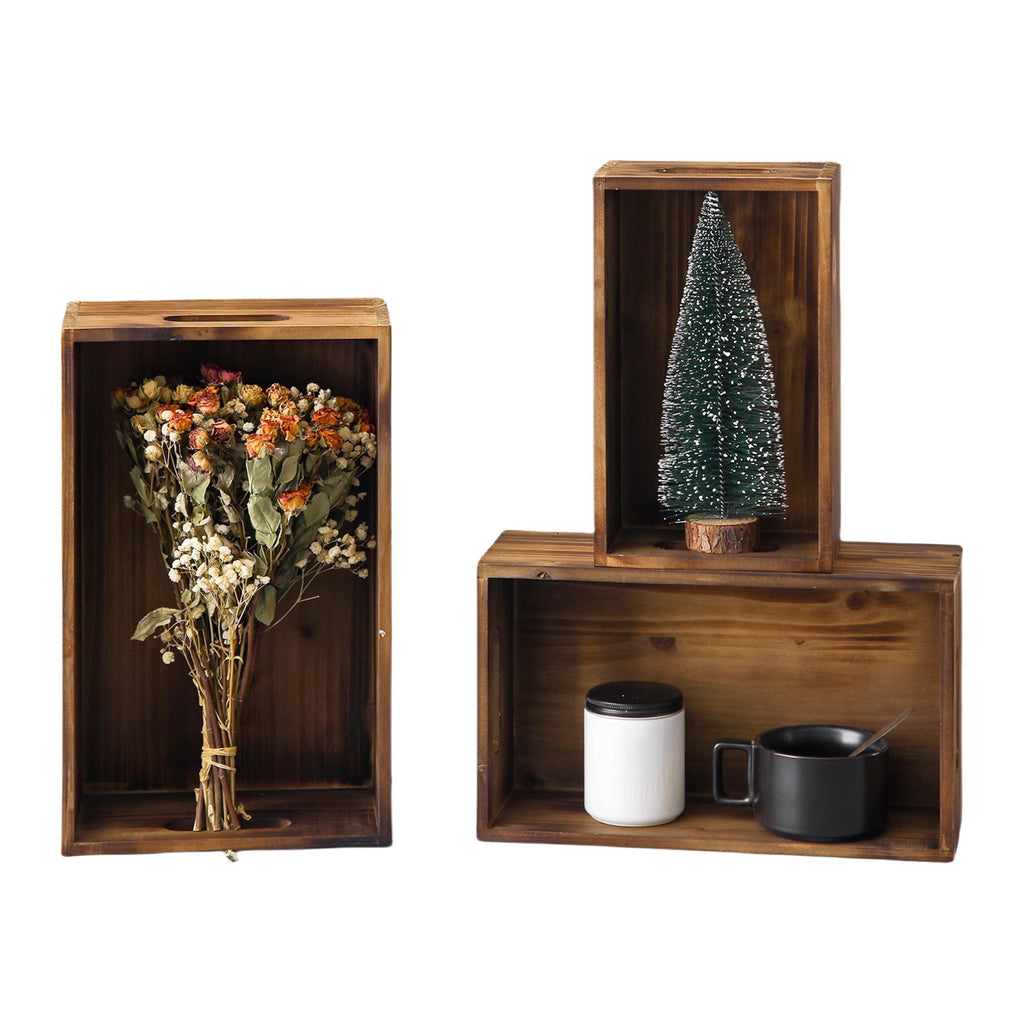 Three distressed fir wood crates with handles, one holding dried flowers, another a miniature Christmas tree, and the third a white jar and black mug.