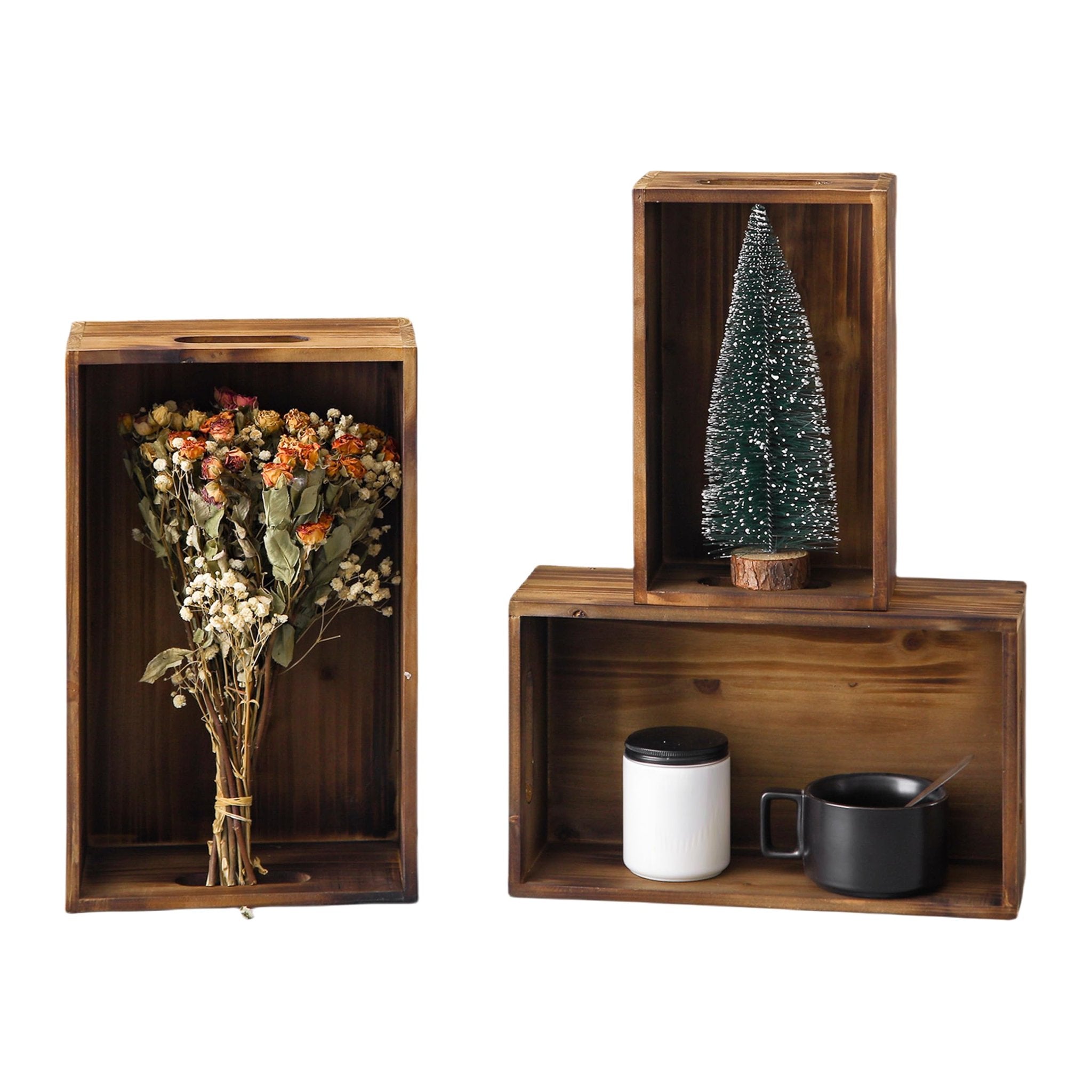 Three distressed fir wood crates with handles, one holding dried flowers, another a miniature Christmas tree, and the third a white jar and black mug.