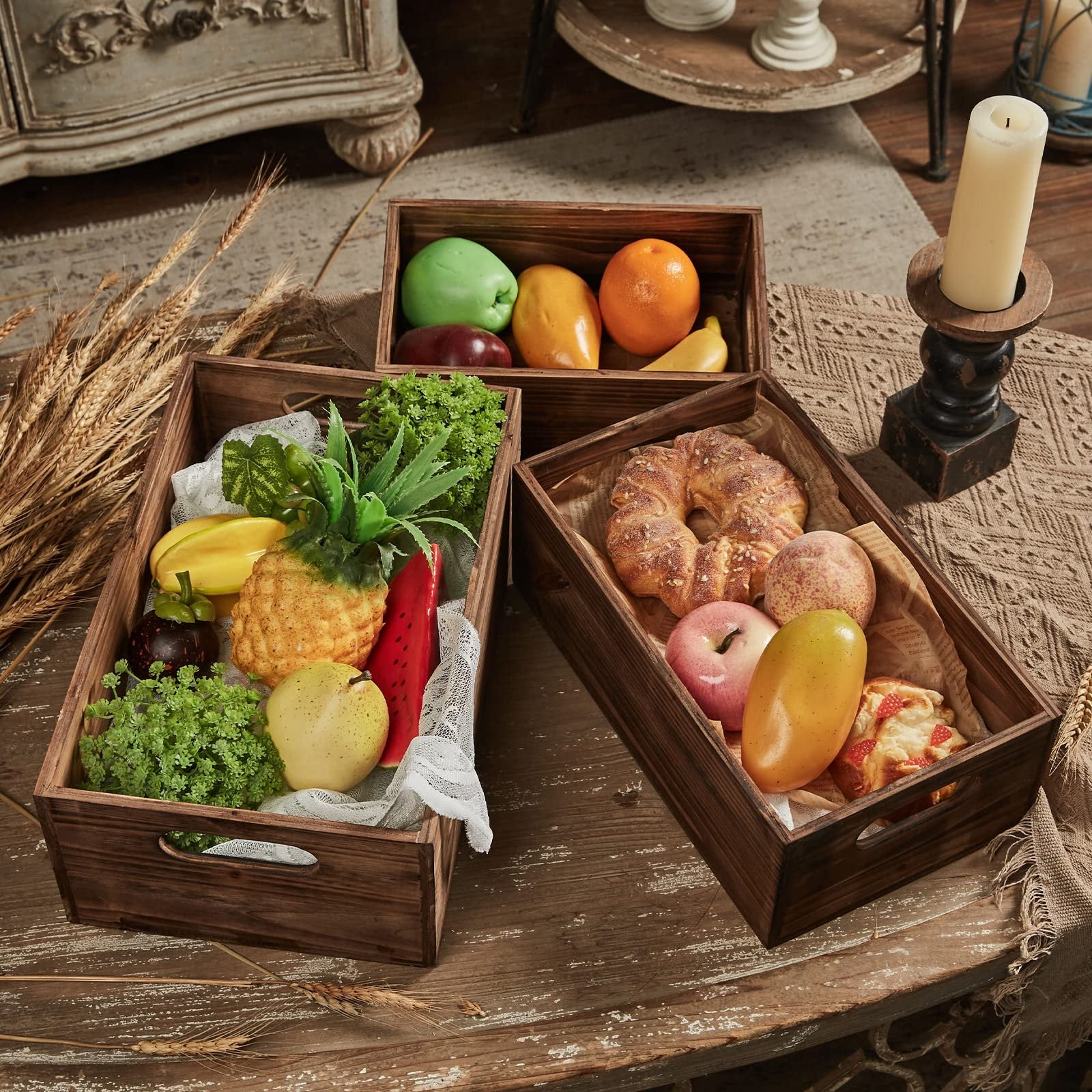 Three distressed fir wood crates filled with artificial fruits, vegetables, and pastries on a rustic table.