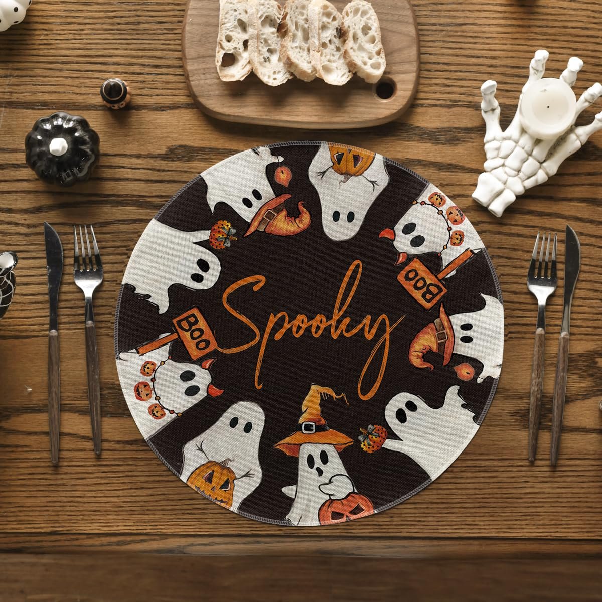Round Halloween placemat with ghosts, pumpkins, and the word Spooky in the center, set on a wooden table with cutlery and bread.
