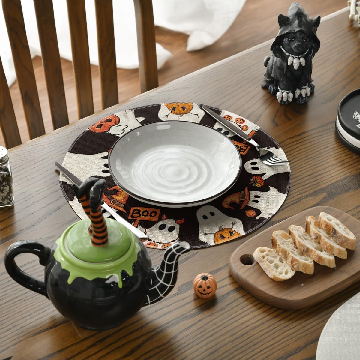 Halloween placemat with ghosts and pumpkins set on a dining table with a plate, fork, knife, and bread.