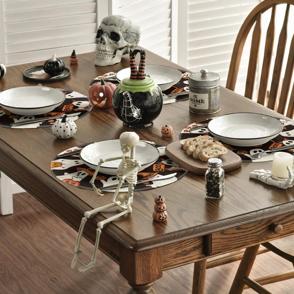 Halloween table setting with spooky ghost placemats, skeleton figure, skull, and pumpkin teapot.