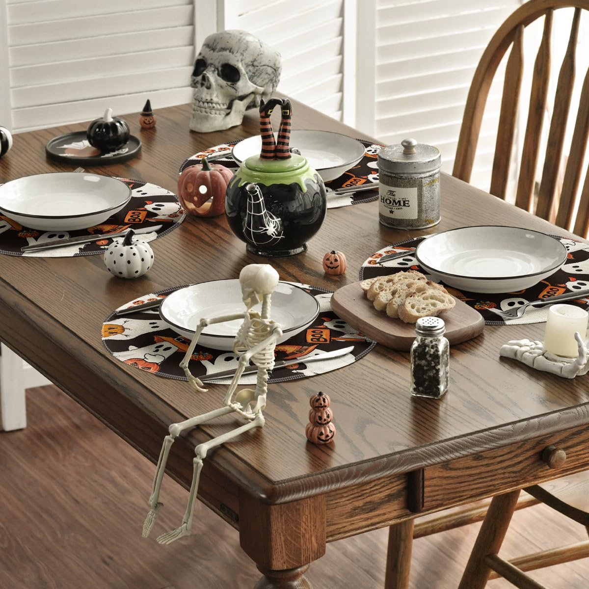 Halloween table setting with spooky ghost placemats, skeleton figure, skull, and pumpkin teapot.