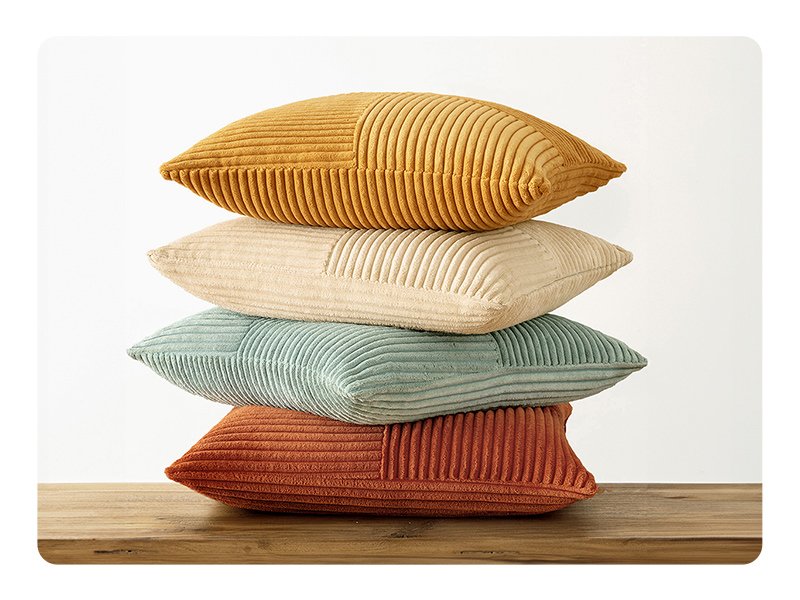 Stack of four corduroy patchwork throw pillow covers in various colors on a wooden surface.