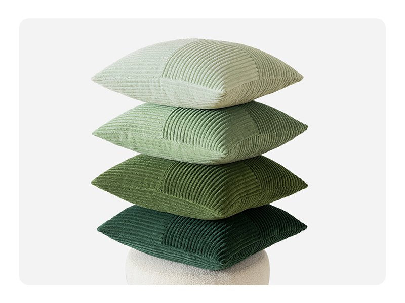 Stack of four corduroy patchwork throw pillow covers in varying shades of green, on a light background.