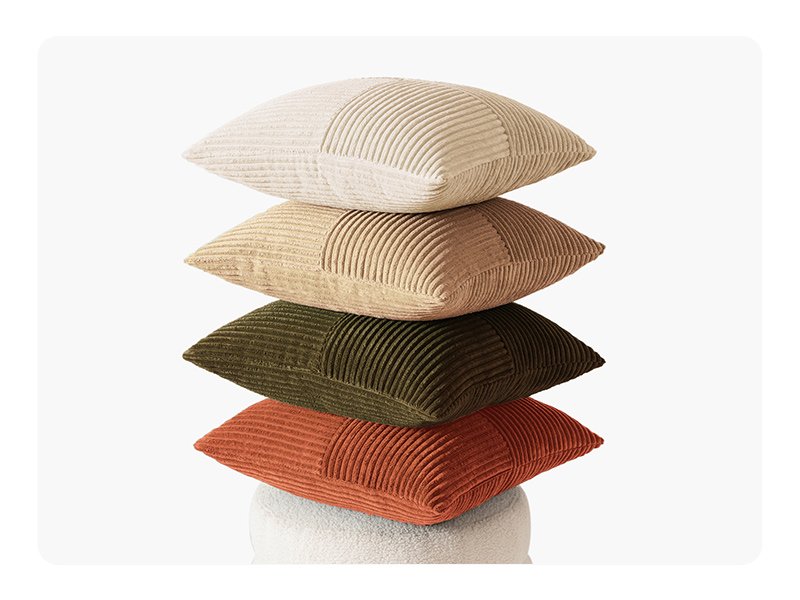 Stack of four corduroy patchwork throw pillow covers in beige, tan, olive green, and rust orange on a white textured surface.