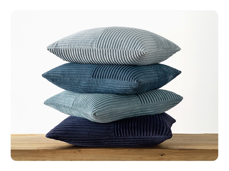 Stack of four corduroy patchwork throw pillow covers in various shades of blue on a wooden surface.