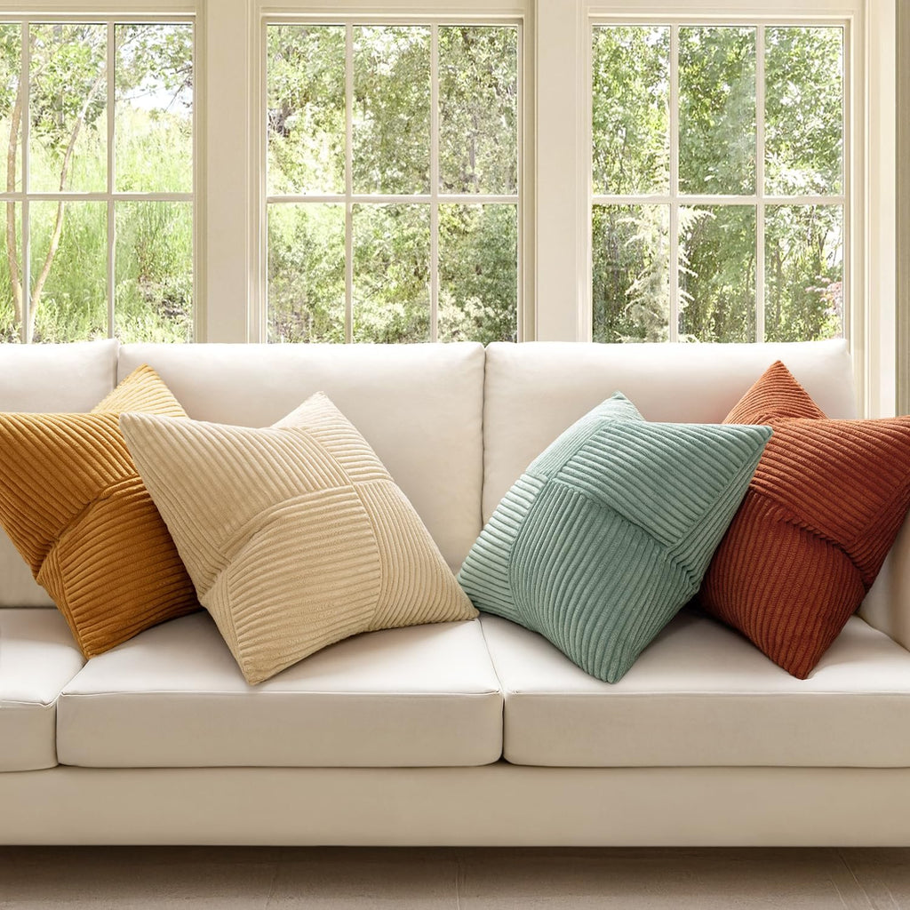 Four corduroy patchwork throw pillow covers in various colors arranged on a white sofa in front of windows.