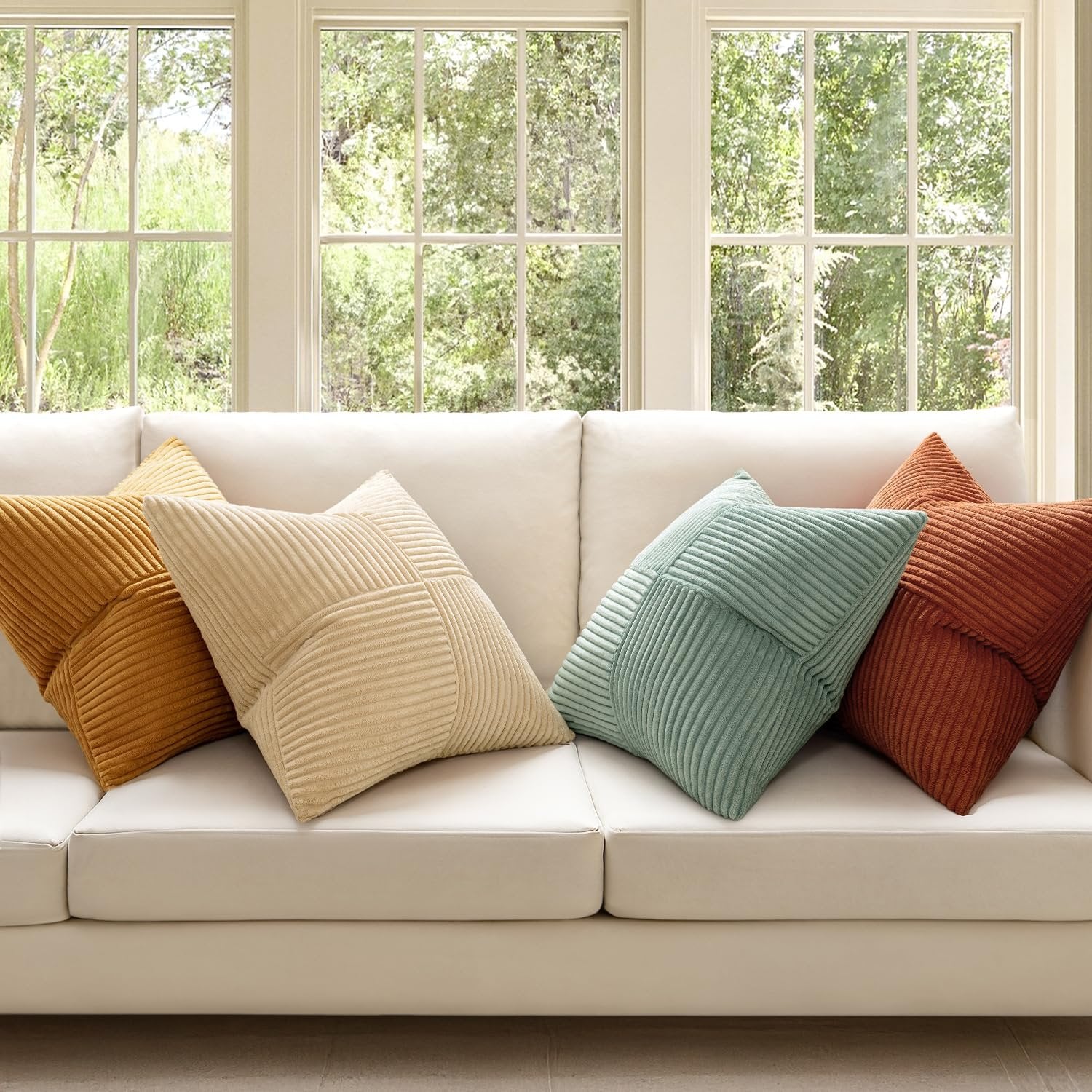 Four corduroy patchwork throw pillow covers in various colors arranged on a white sofa in front of windows.