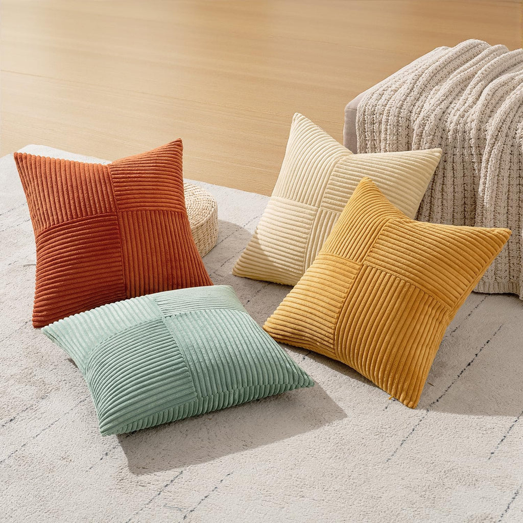 Four corduroy patchwork throw pillow covers in teal, orange, yellow, and cream arranged on a rug.