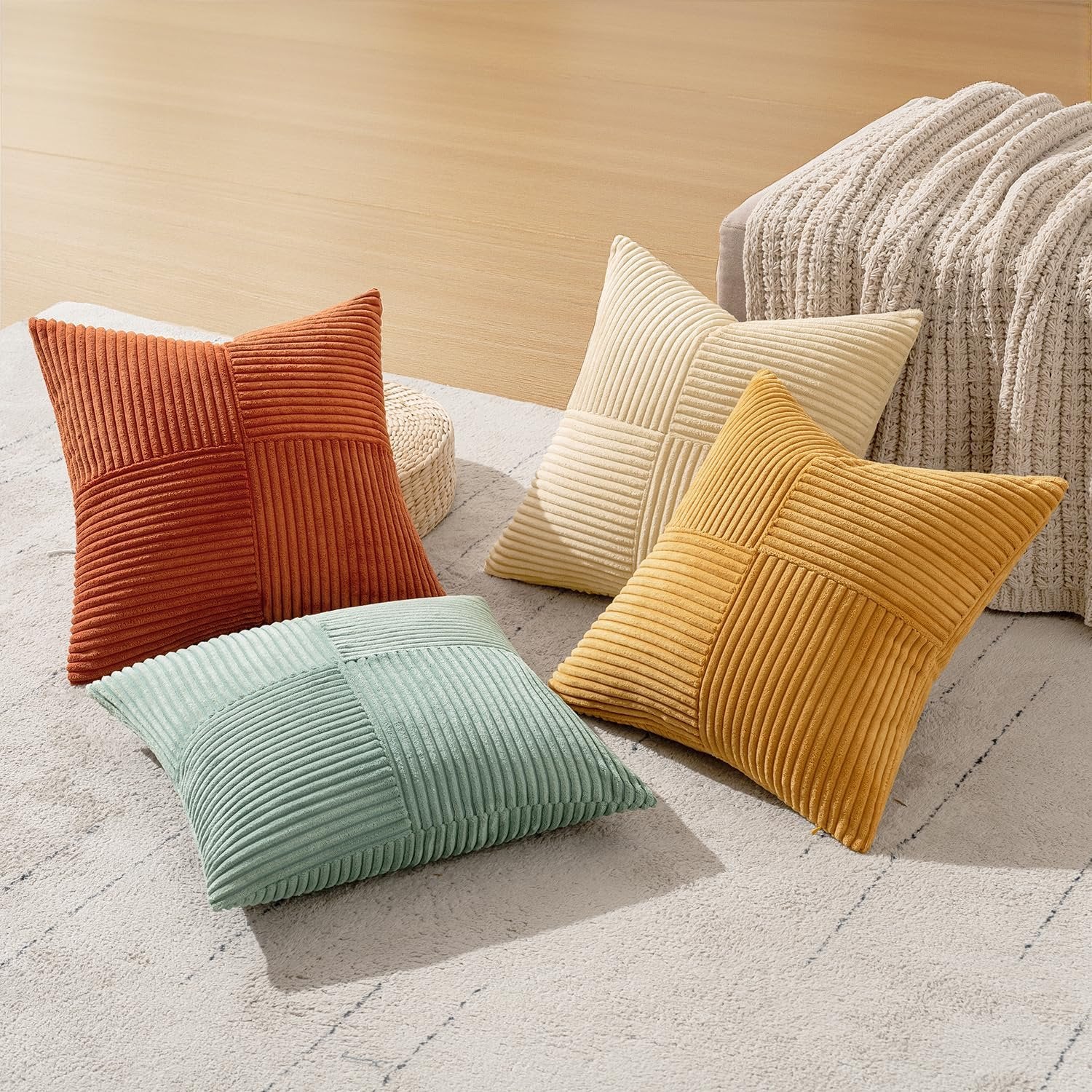 Four corduroy patchwork throw pillow covers in teal, orange, yellow, and cream arranged on a rug.