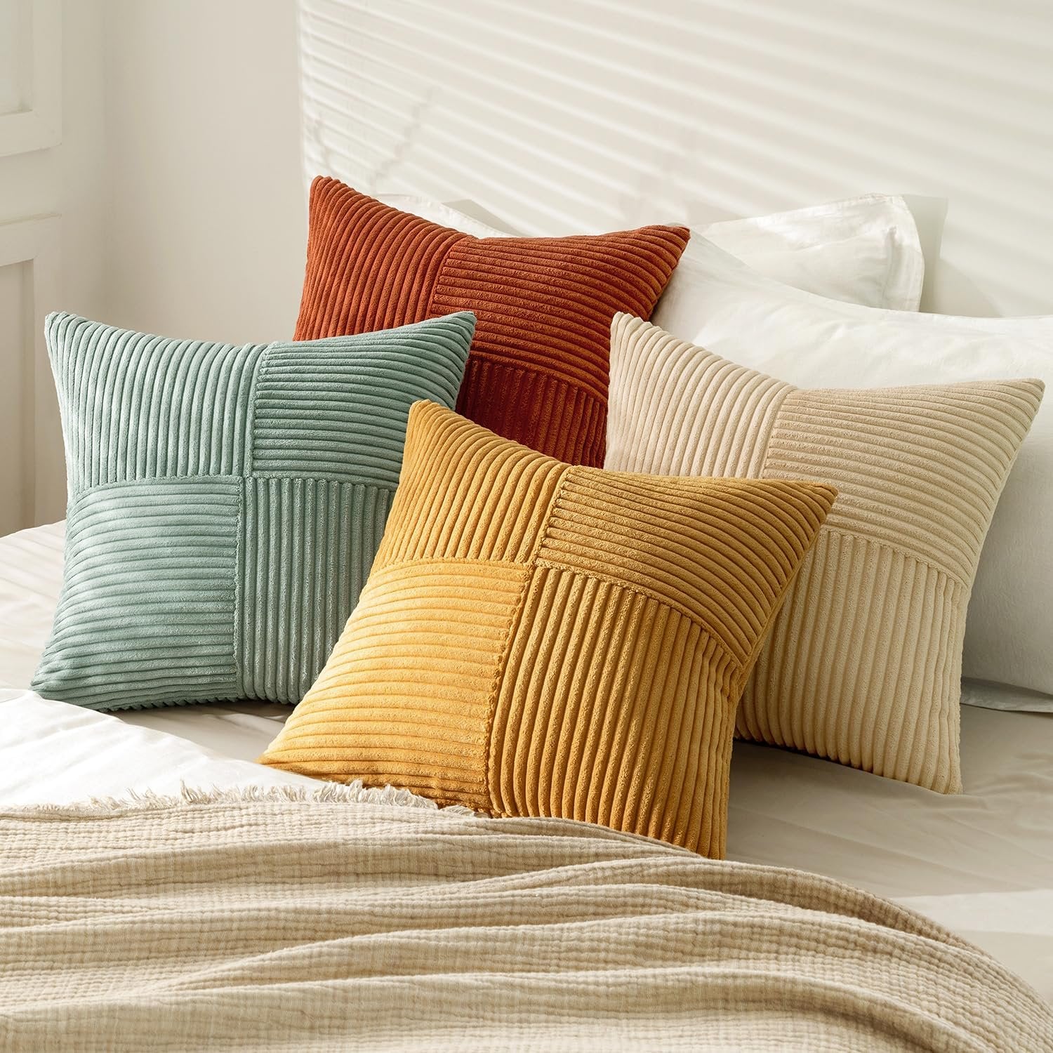 Set of five corduroy patchwork throw pillow covers in teal, rust, yellow, and beige arranged on a bed with a textured throw blanket.