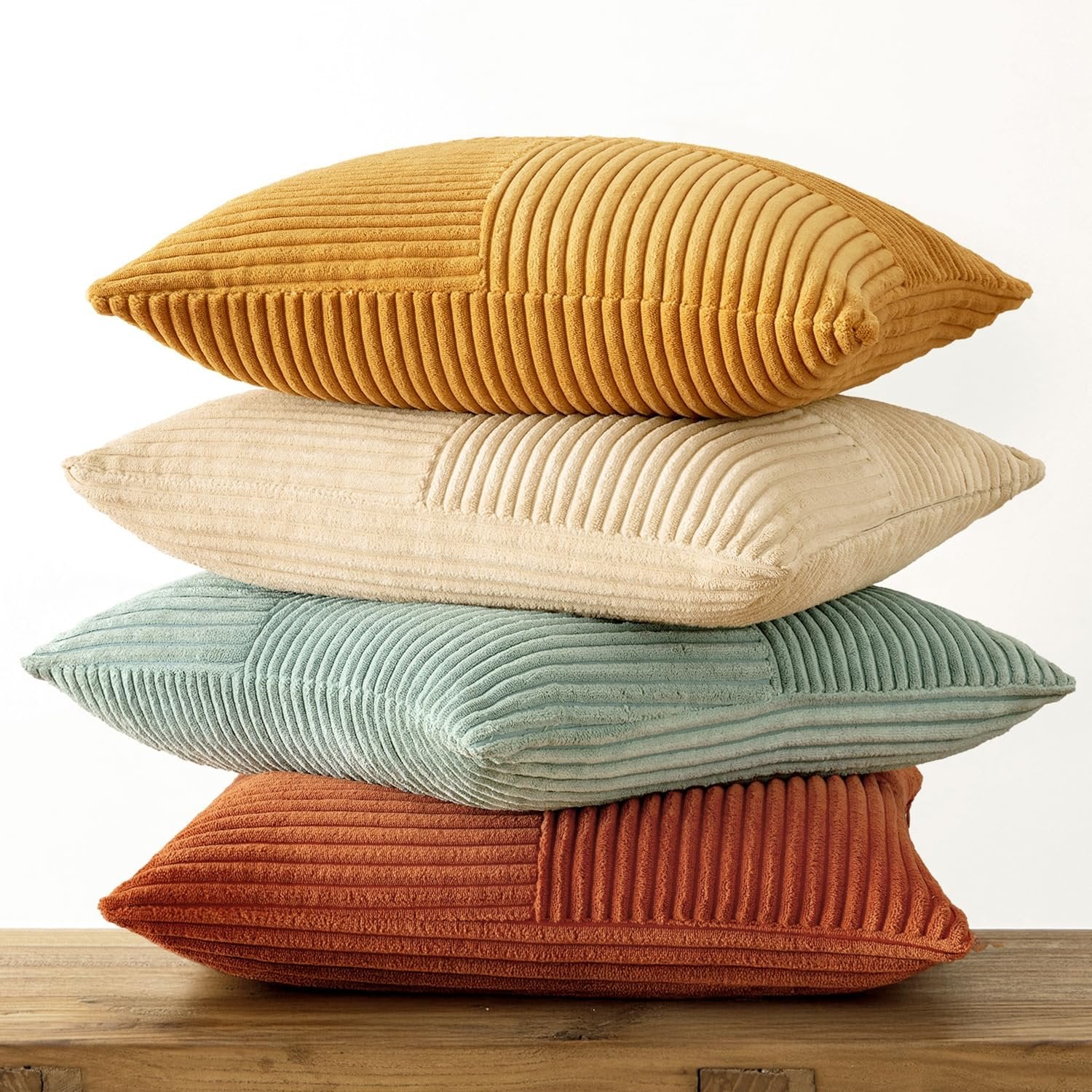 Stack of four corduroy patchwork throw pillow covers in various colors on a wooden surface.