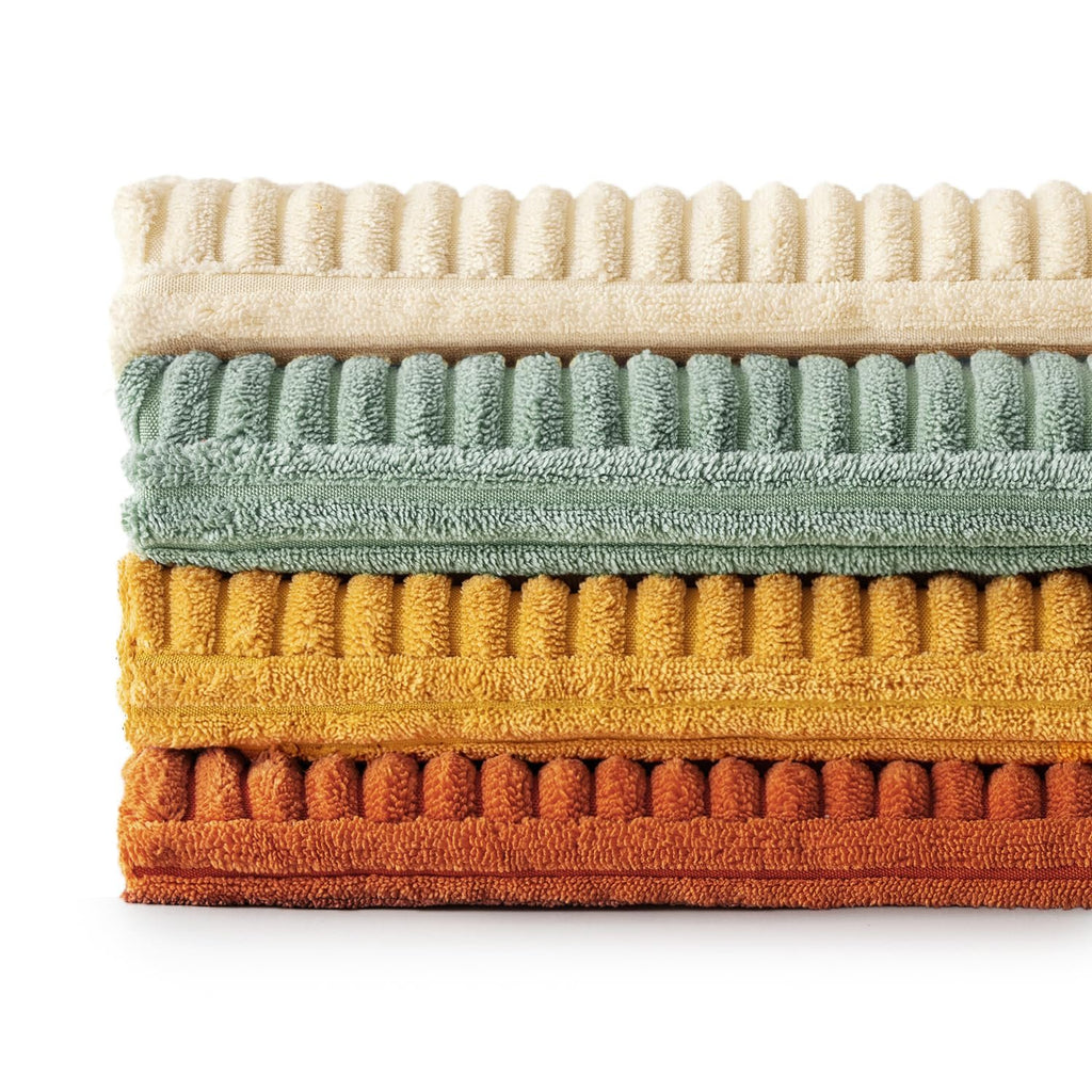Stack of four corduroy patchwork throw pillow covers in cream, sage green, mustard yellow, and rust orange, showing ribbed texture.