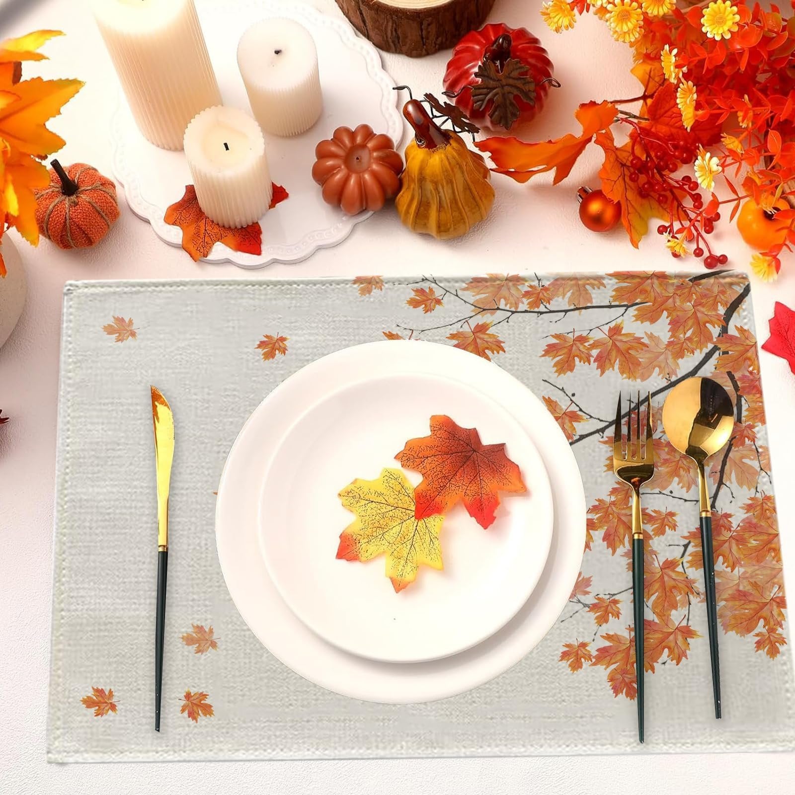 Autumn placemat with maple leaves and branches, set with white plates and gold cutlery.