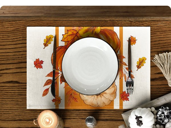 Fall placemat with pumpkins and autumn leaves, set with a plate and cutlery on a wooden table.