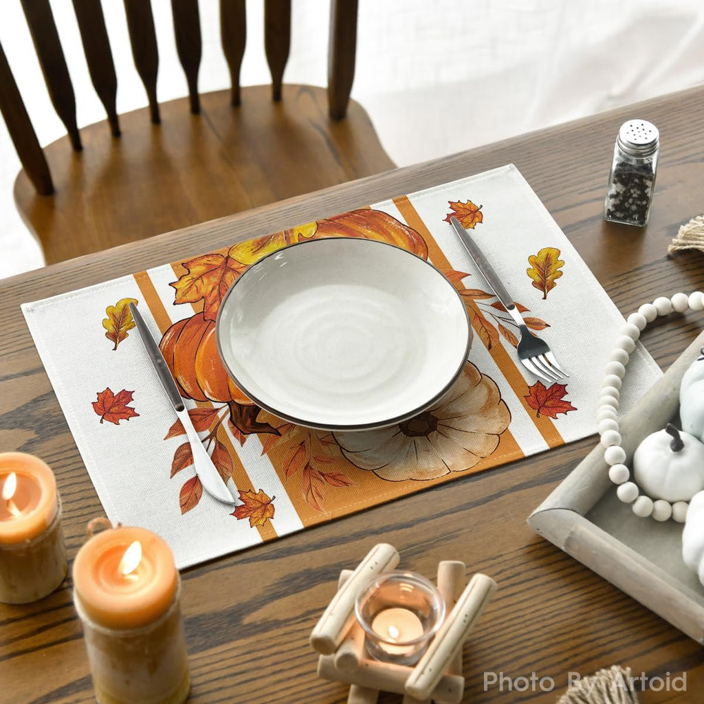 Fall placemat with pumpkins and leaves, set with a plate, fork, and knife on a wooden table with candles.