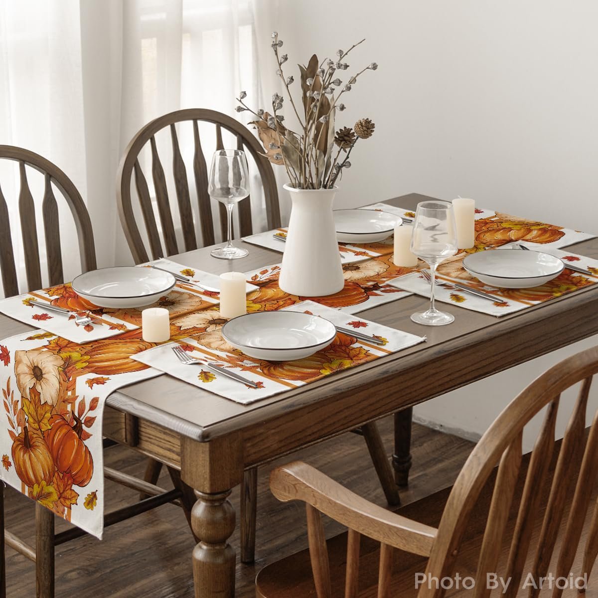 Set of four fall pumpkin and leaf placemats arranged on a dining table with plates, glasses, and candles.