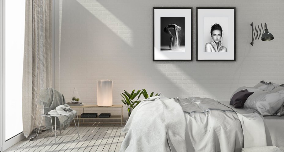 Two framed black and white art prints hanging on a white brick wall above a bed in a bedroom.