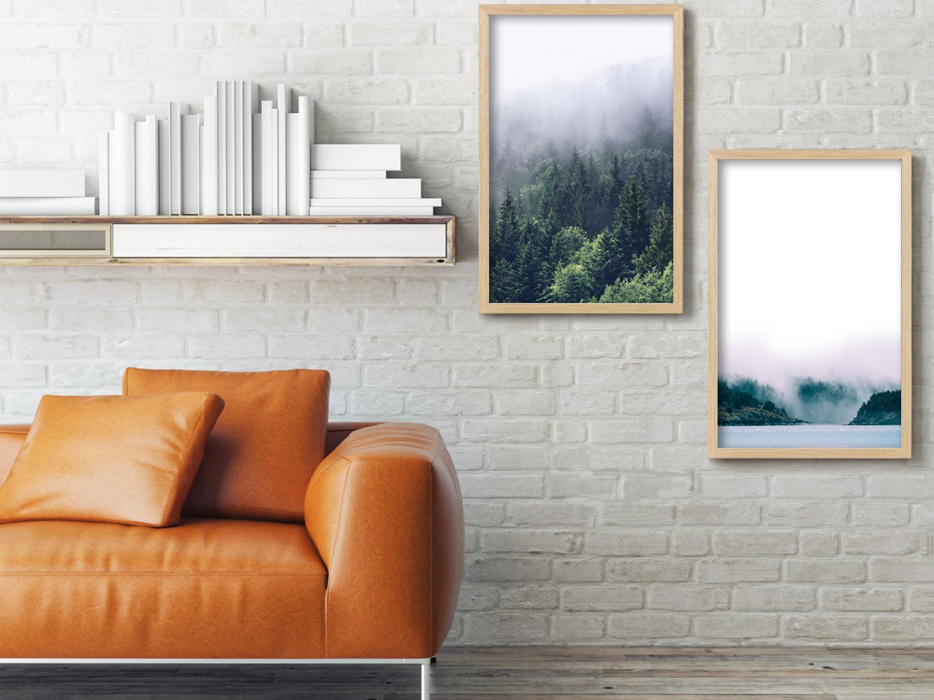 Two framed nature prints hanging on a white brick wall above a tan leather sofa with pillows.