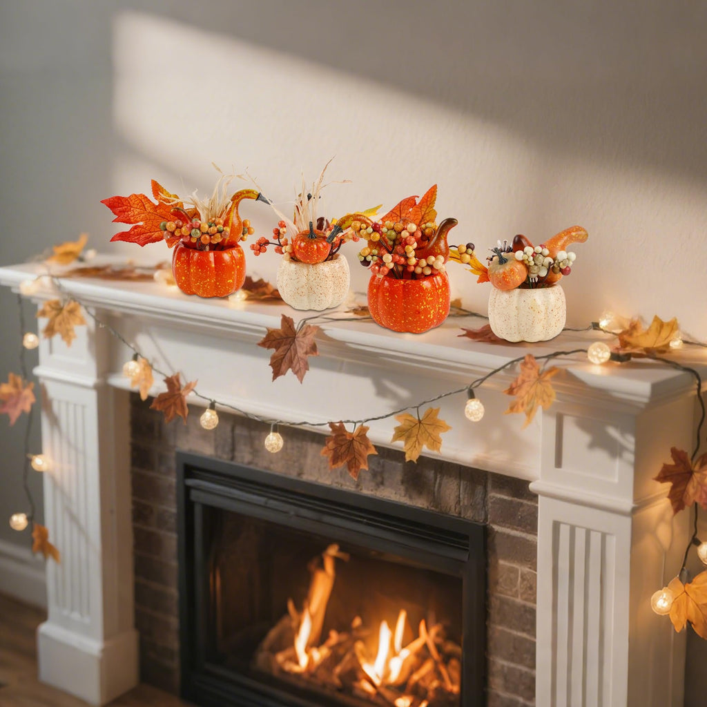 Four fall-themed artificial pumpkin centerpieces with berries and leaves arranged on a white mantelpiece above a fireplace, with a string of leaf-shaped lights.