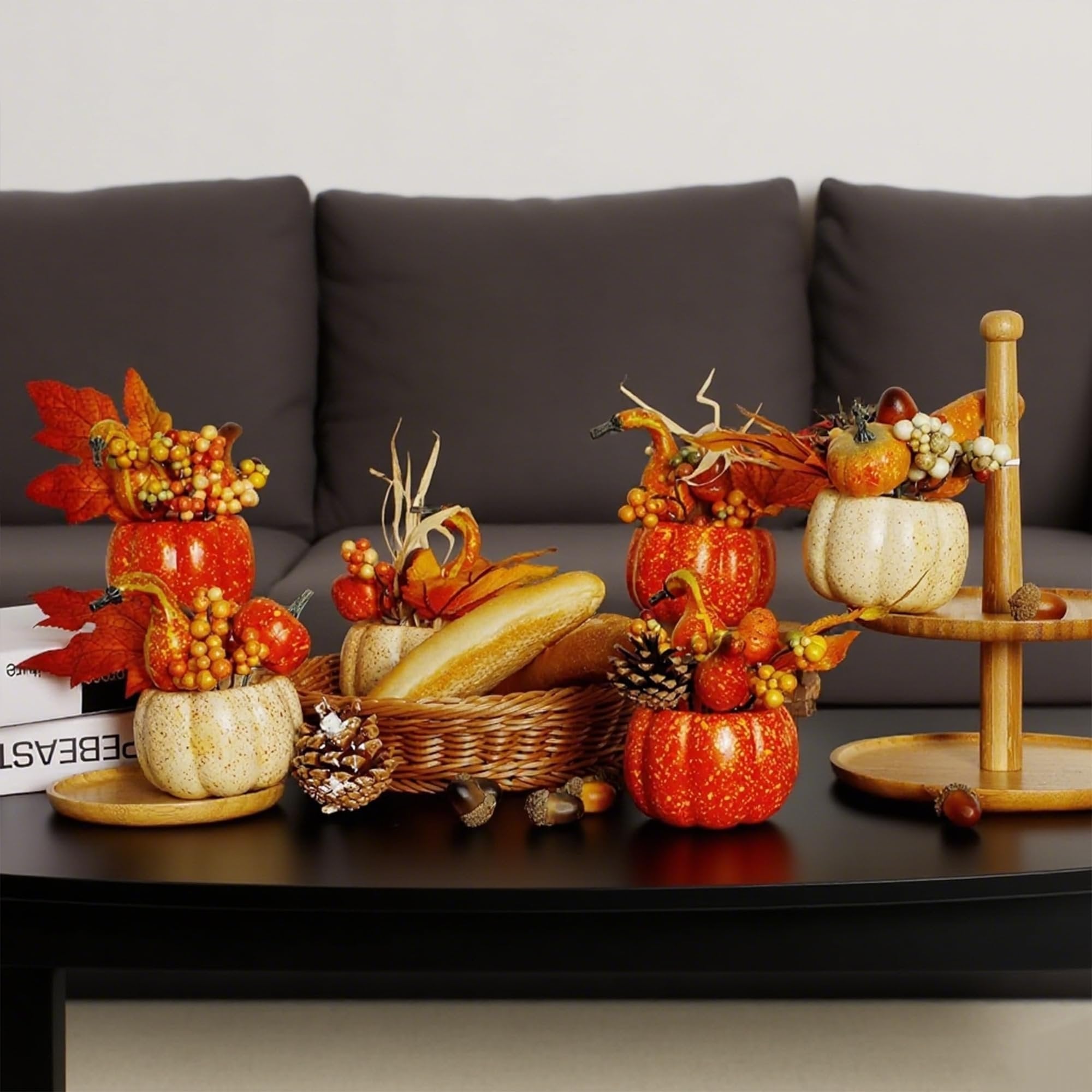 Set of artificial fall pumpkins, berries, and pine cones arranged on a coffee table with a basket of bread and a tiered stand.
