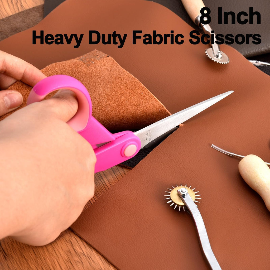 Close-up of pink-handled fabric scissors cutting brown leather, with leathercraft tools visible.