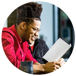 Man in red shirt smiling while reading a blank card, seated at a table with another person.