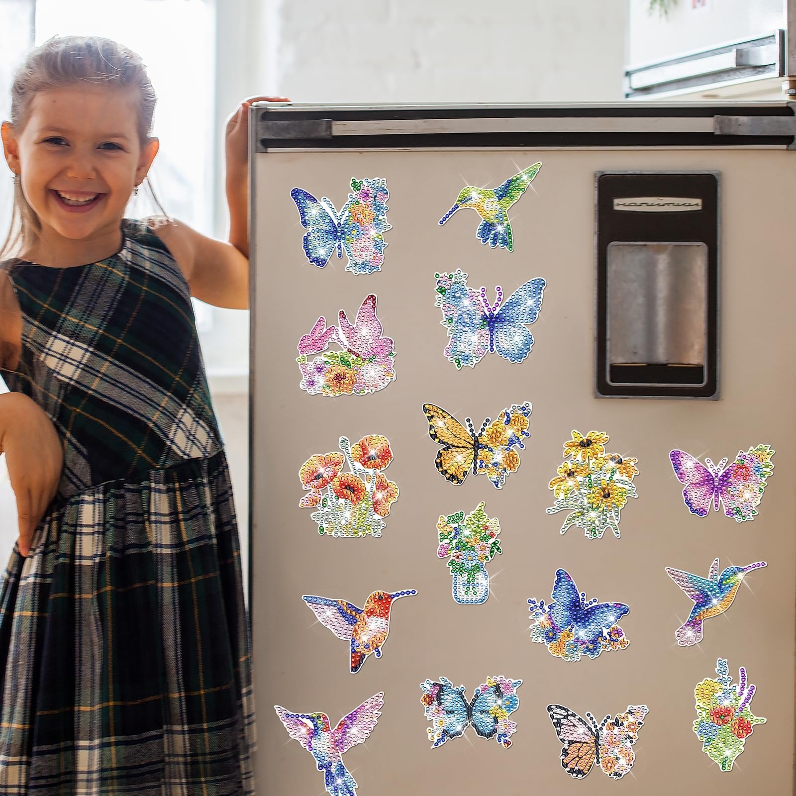 Smiling girl in plaid dress stands by a refrigerator adorned with colorful diamond art butterfly and hummingbird magnets.