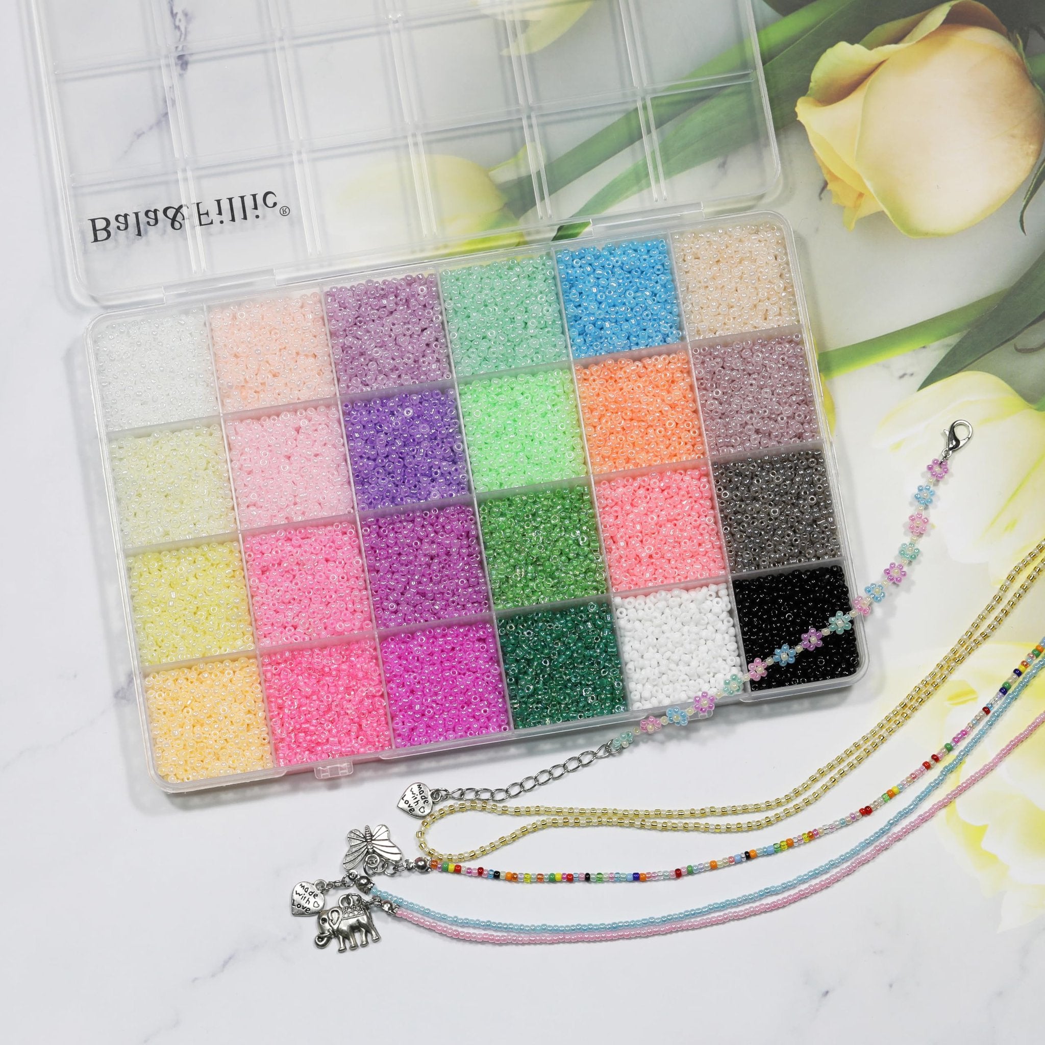 Clear storage box filled with 24 colors of small glass seed beads, with finished jewelry pieces to the side.