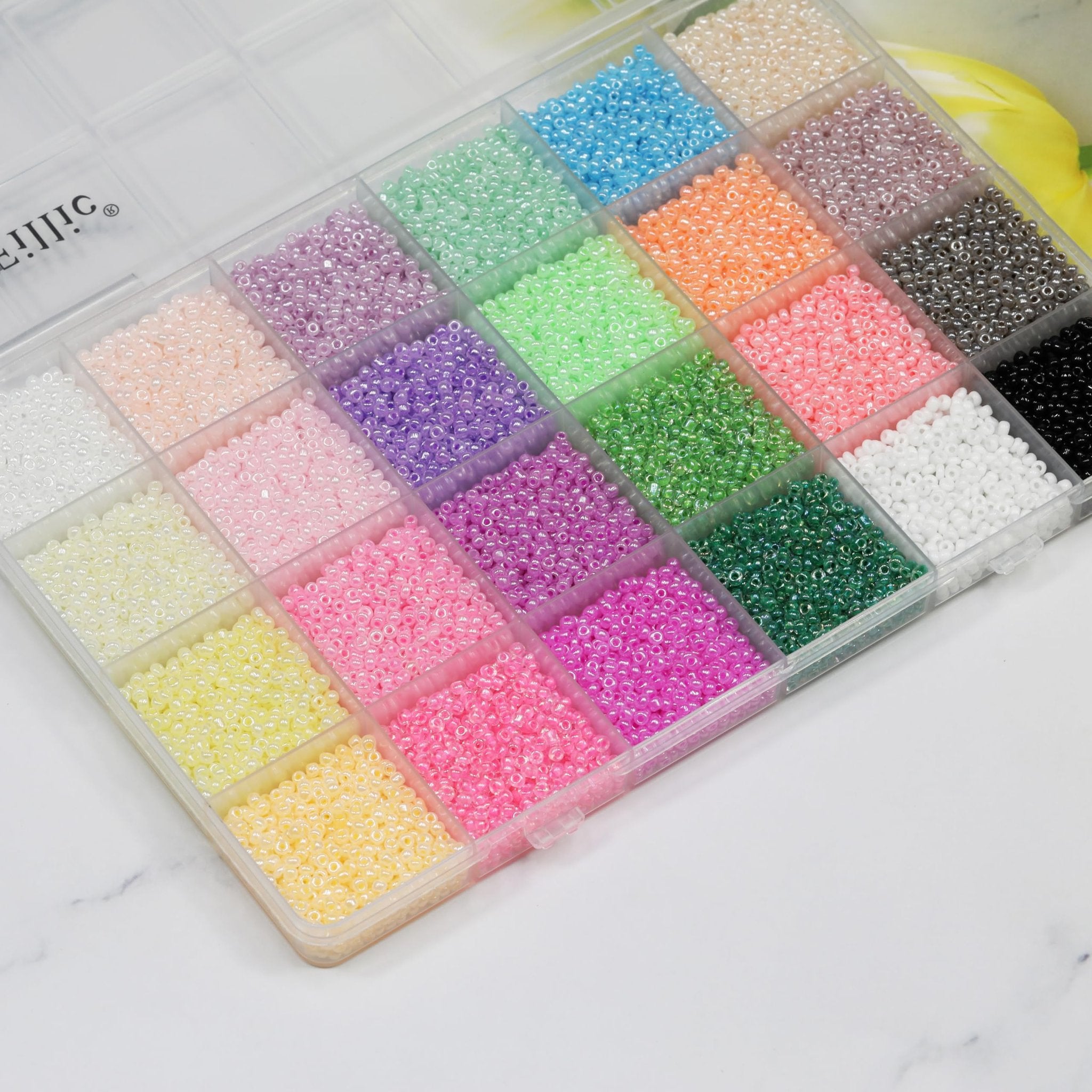Clear storage box filled with 24 colors of small glass seed beads for jewelry making and crafts.