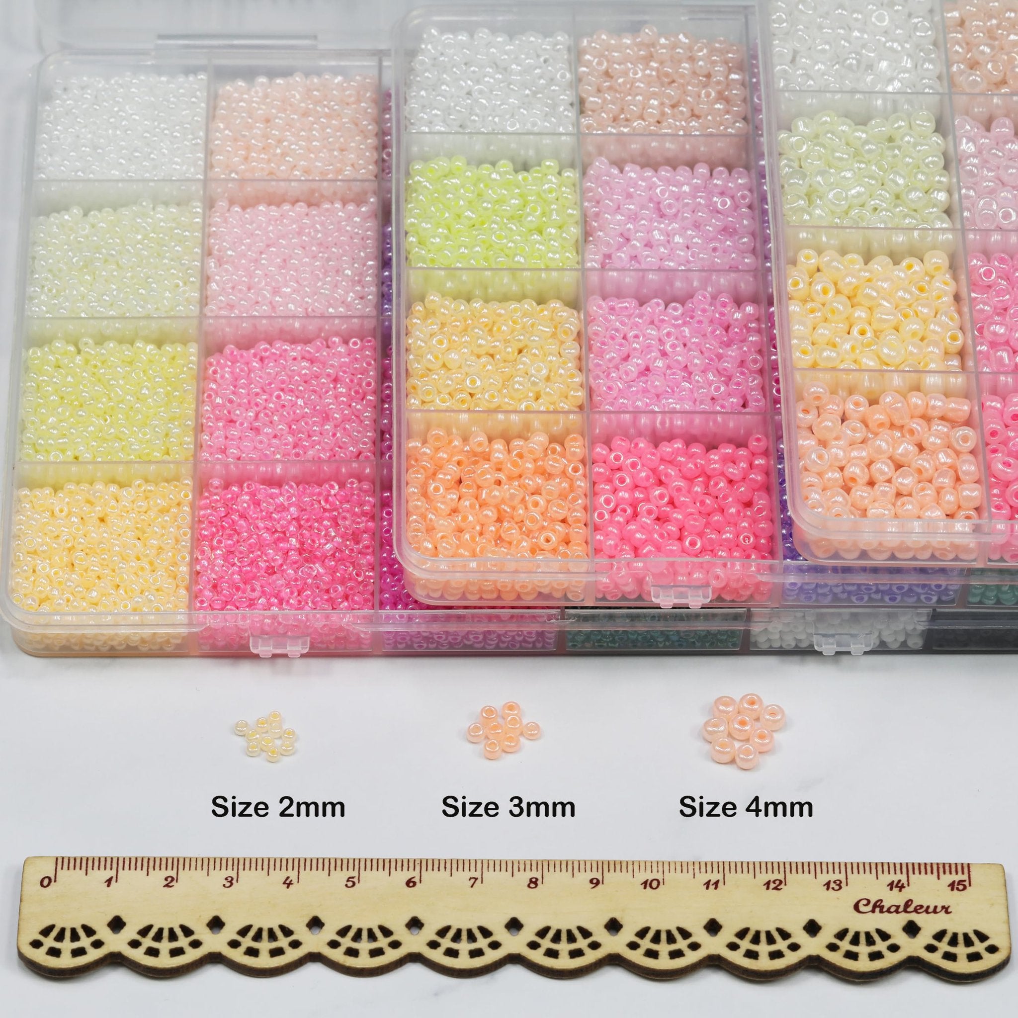 Assortment of colorful glass seed beads in a divided storage box, with size references and a ruler.