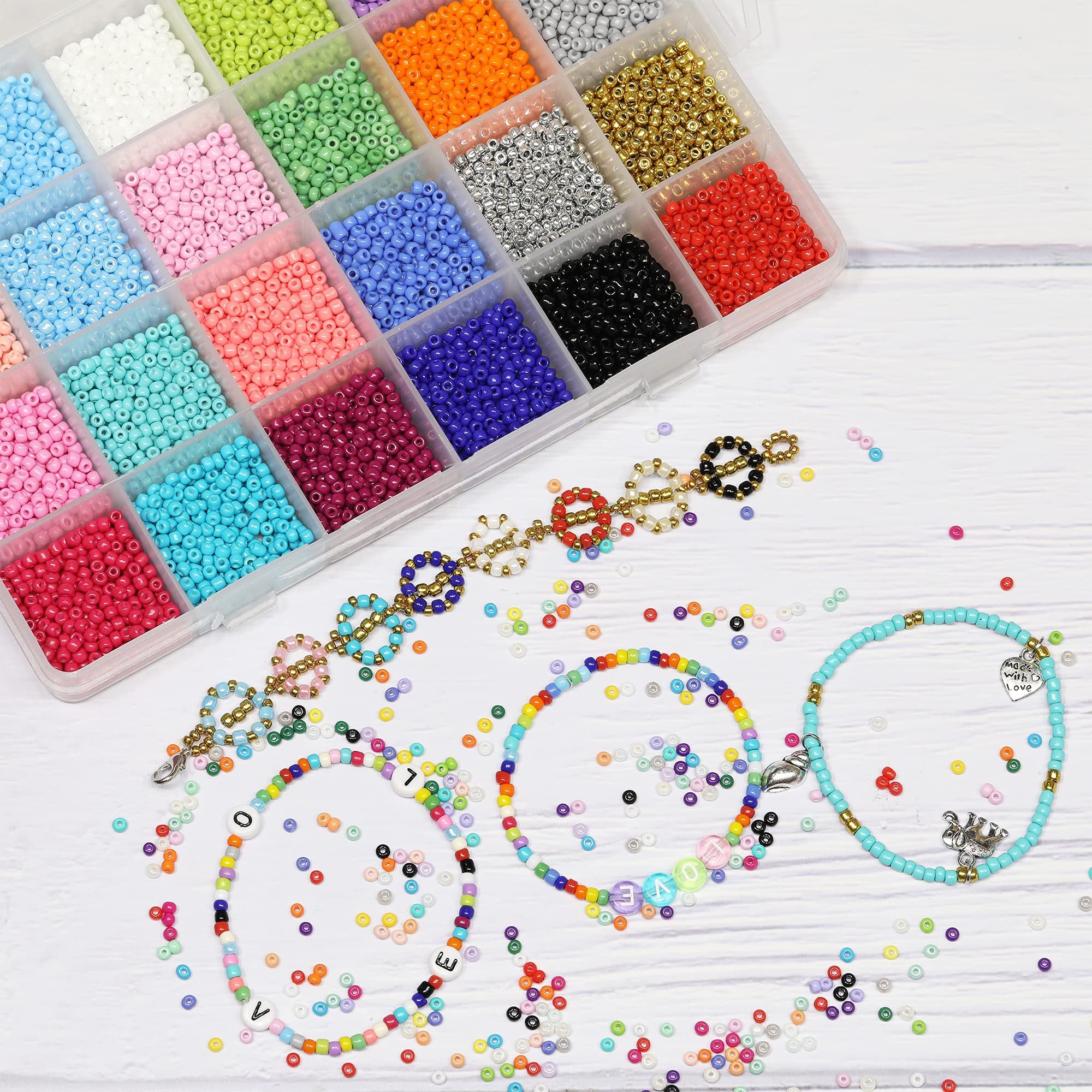 Assorted colorful seed beads in a divided organizer box with finished bracelets and scattered beads on a white wooden surface.