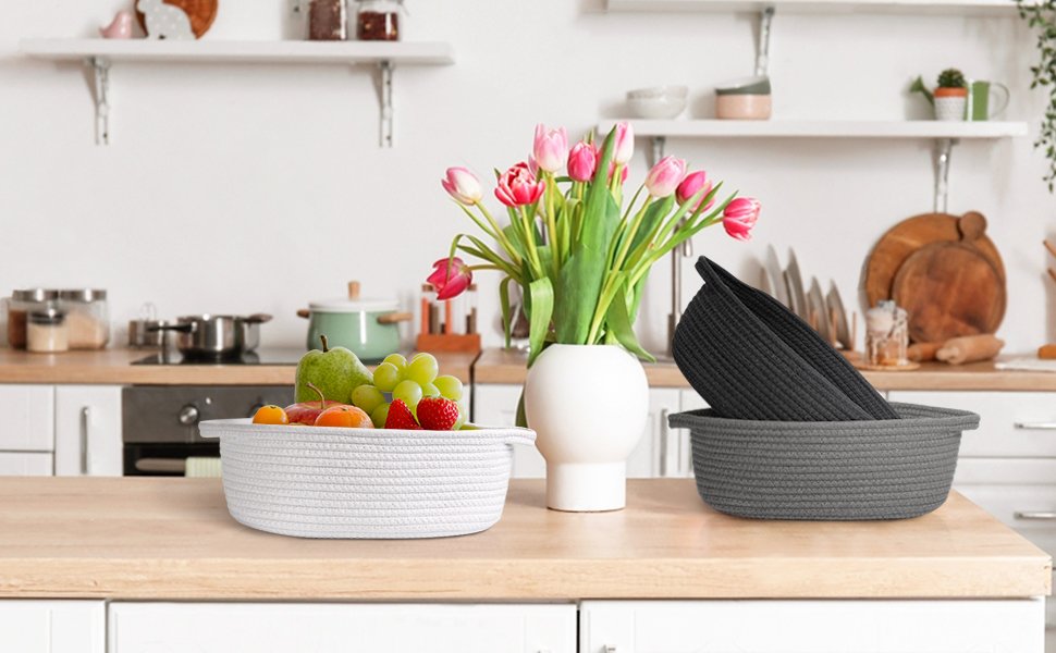 Two woven cotton rope baskets, one white filled with fruit and one grey with a black basket inside, on a kitchen counter.