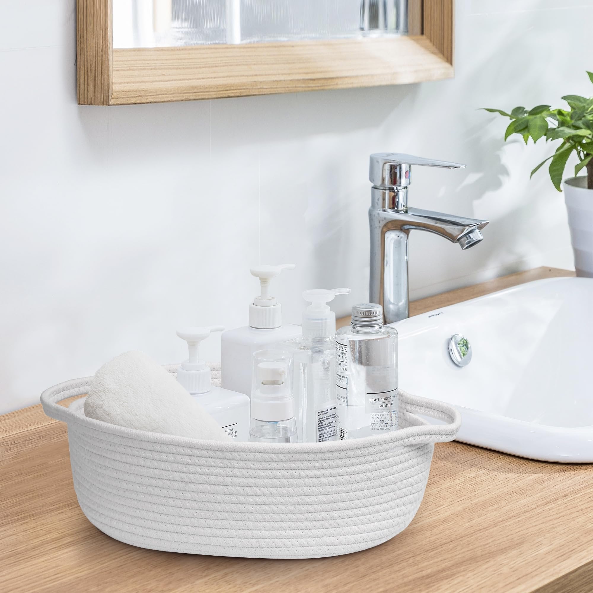 Woven cotton rope basket with handles holding a folded white towel and various toiletries on a bathroom counter next to a sink.