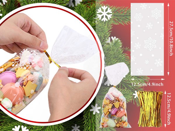 Hands tying a gold twist tie on a clear cellophane treat bag filled with candies and cookies, with snowflake pattern.