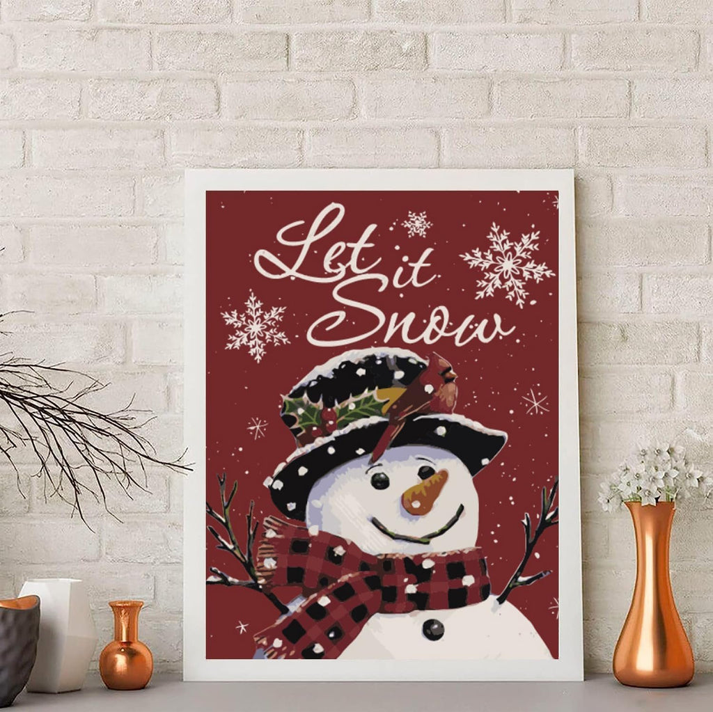 Framed snowman painting with 'Let it Snow' text and snowflakes, set against a white brick wall.
