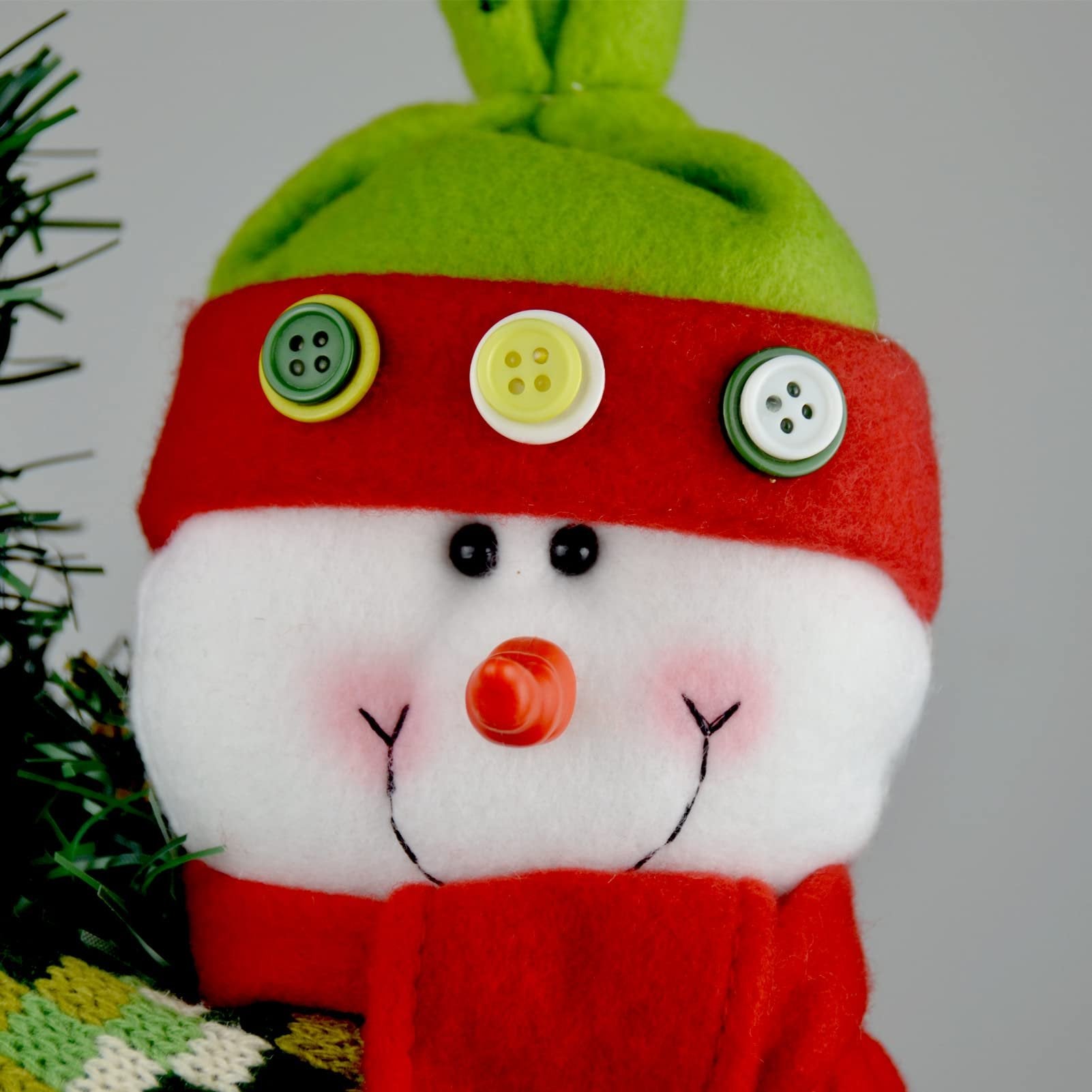 Close-up of a plush snowman Christmas tree topper's face with a green hat, red scarf, and buttons.