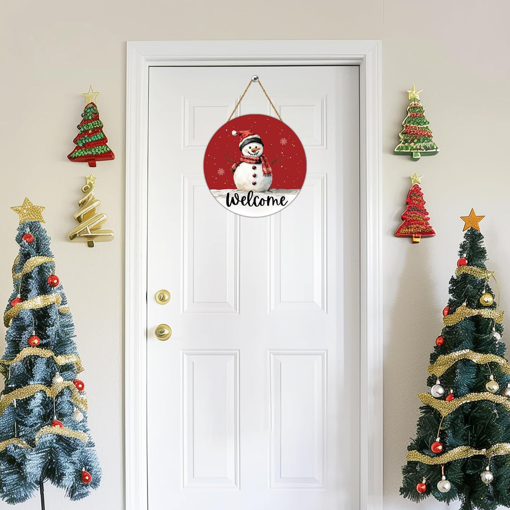 Round wooden snowman welcome door hanger with red background, hanging on a white door with Christmas decorations.
