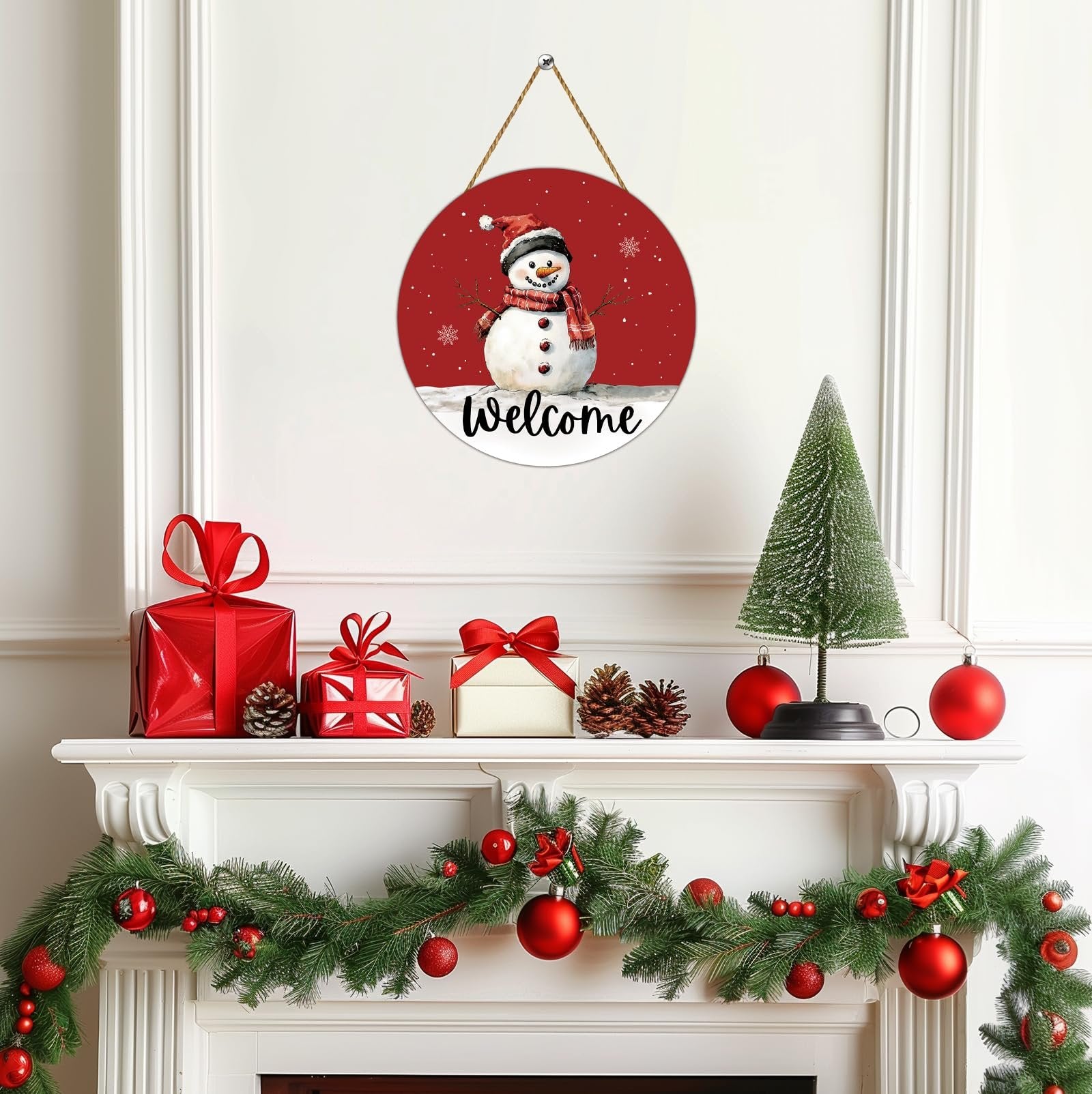 Round wooden snowman welcome door hanger with red background, displayed on a mantelpiece with Christmas decorations.