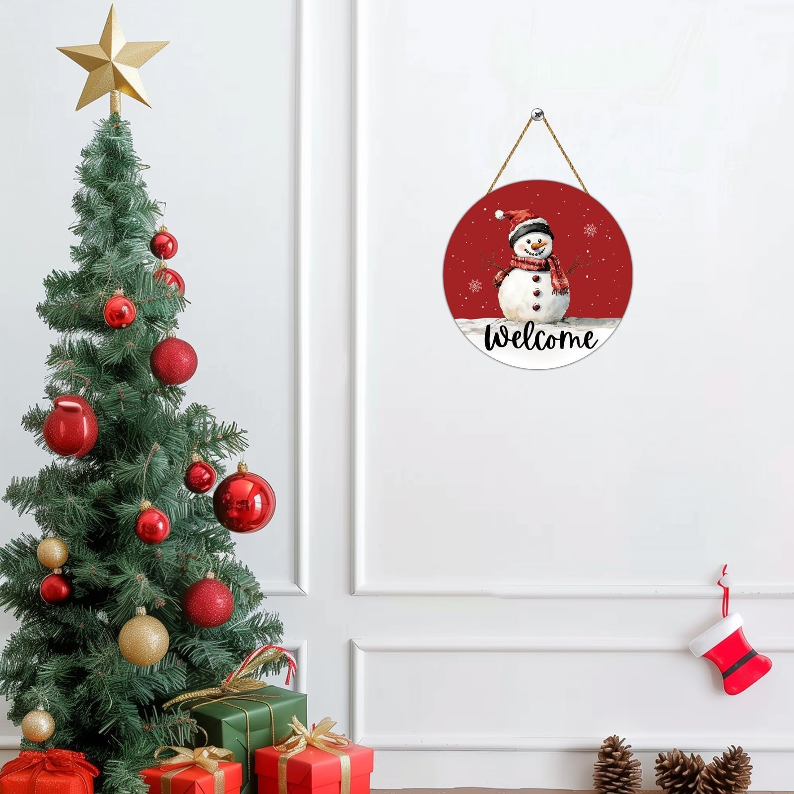 Round wooden snowman welcome door hanger with red scarf and hat, displayed next to a decorated Christmas tree.