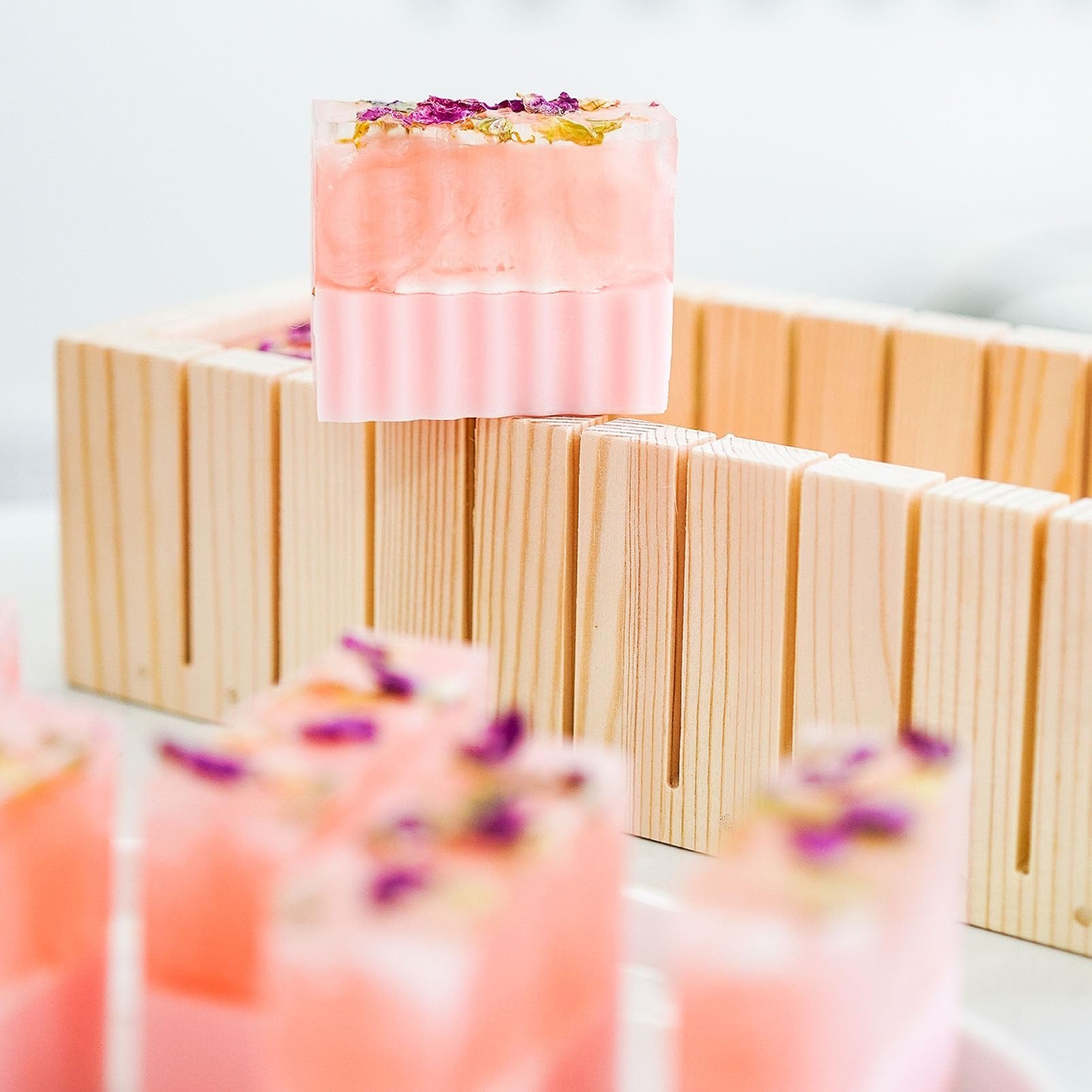 Pink soap bars with dried flowers on top, resting on a wooden soap cutting mold