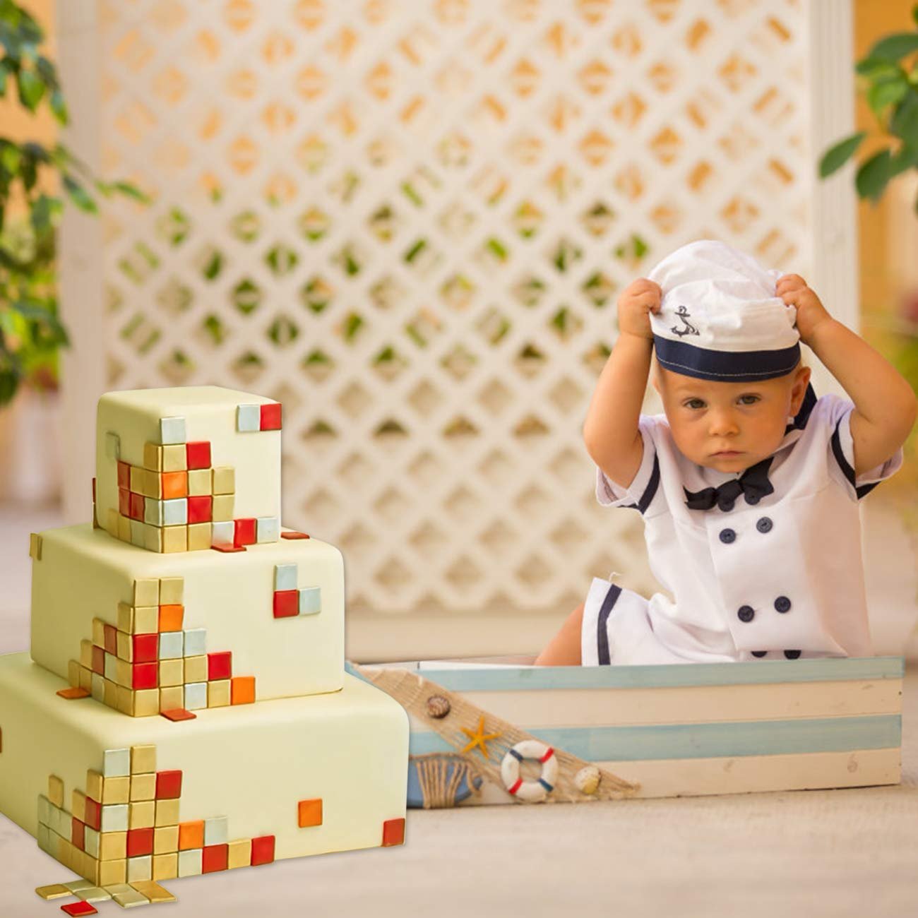 Baby in sailor outfit sitting in a boat next to a tiered cake decorated with colorful squares