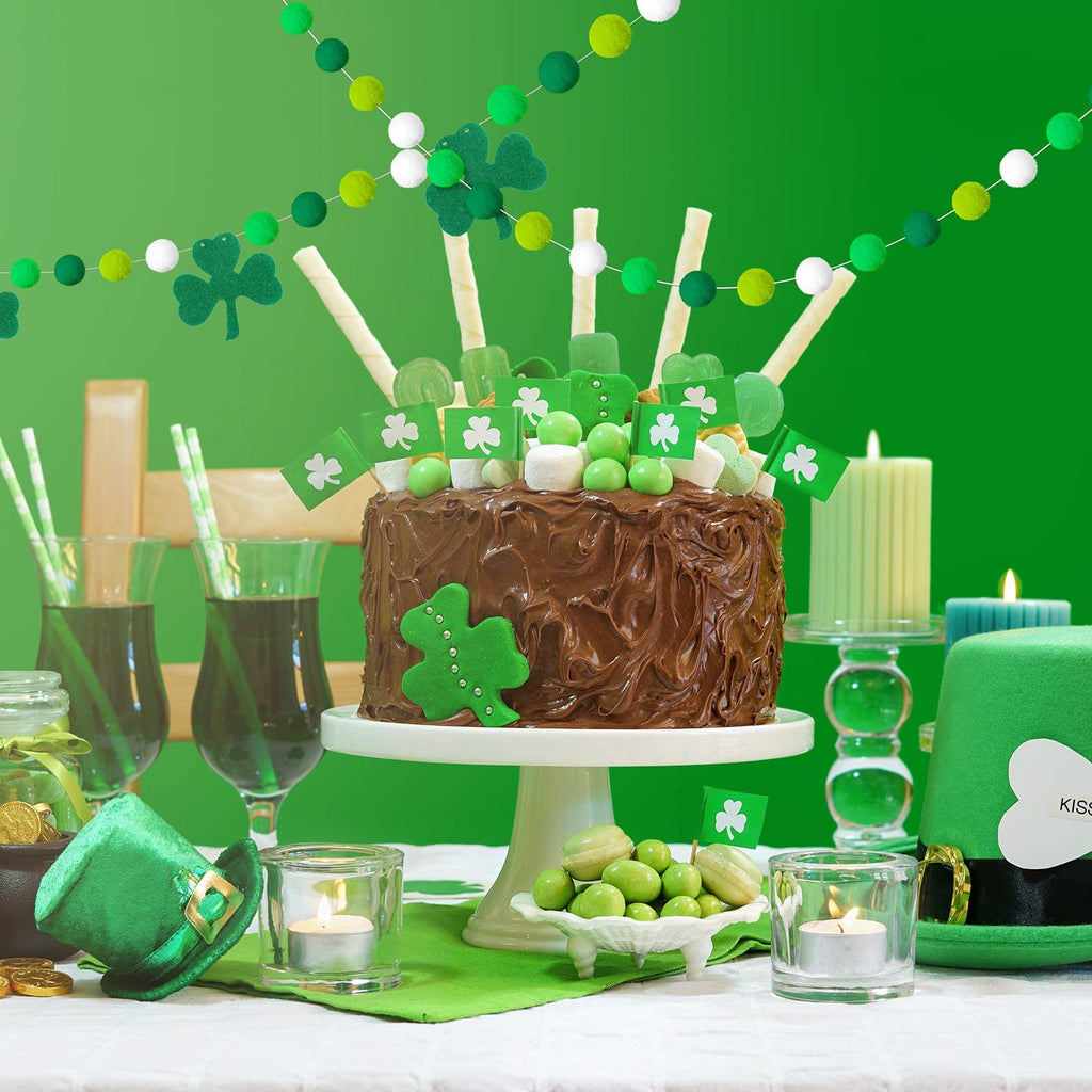 St. Patrick's Day cake decorated with green shamrocks, candy, and small flags, with pom pom garlands and festive decor.