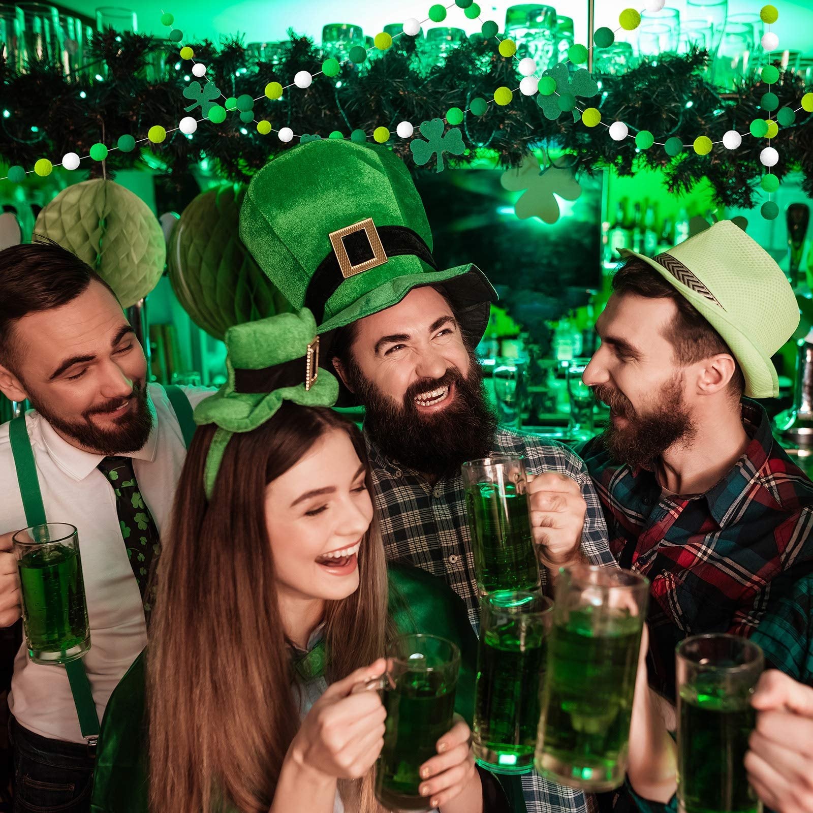 Four people in St. Patrick's Day attire toasting with green drinks at a bar, with festive green and white garland overhead.