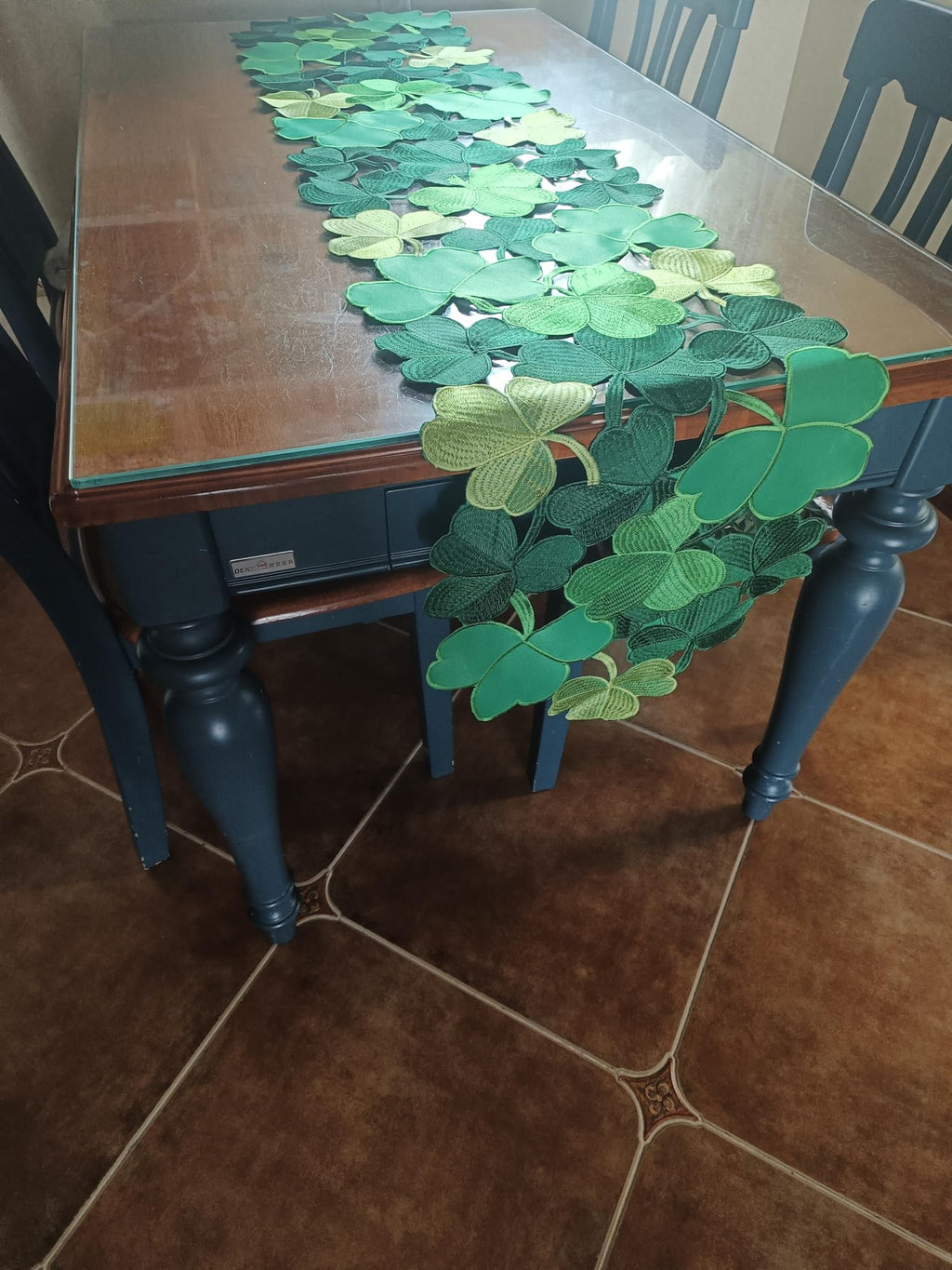 Green embroidered shamrock table runner draped across a wooden table with chairs visible