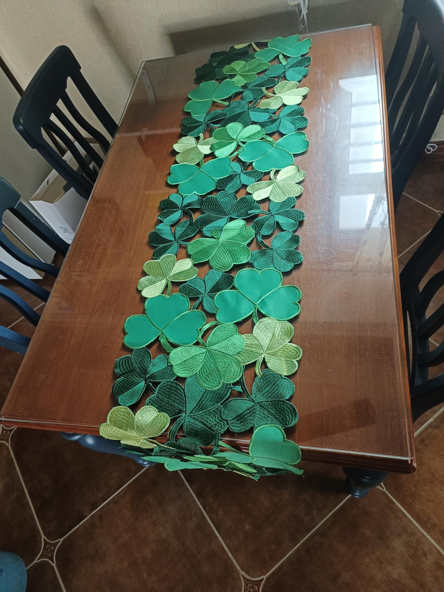 St. Patrick's Day table runner with embroidered clover cutouts laid on a wooden table with chairs.